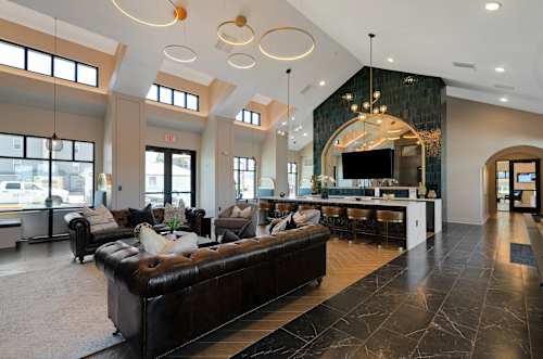 A large, modern living room with a black leather couch and a bar area.