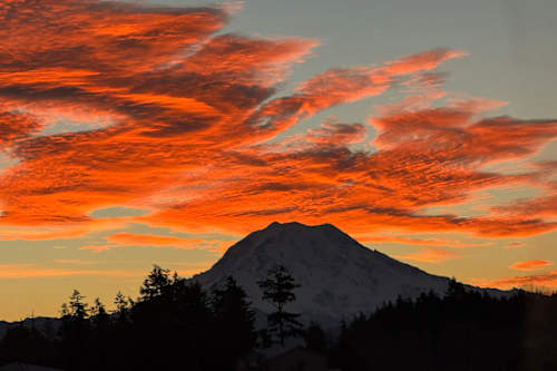 A mountain with a snow cap under a sky with orange clouds. at Madison Sierra Sun, Washington, 98374