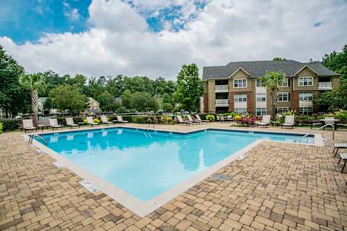 A large swimming pool surrounded by a brick patio and lounge chairs.
