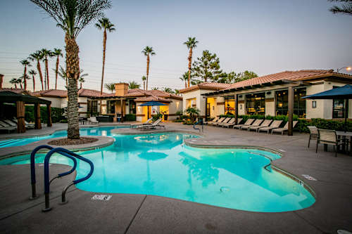 A pool surrounded by palm trees and lounge chairs.