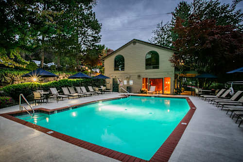 A pool surrounded by lounge chairs and umbrellas in front of a house.