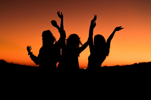 three people silhouetted against a sunset with their hands in the air