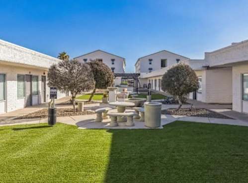 A sunny day in a courtyard with a fountain, trees, and buildings in the background.