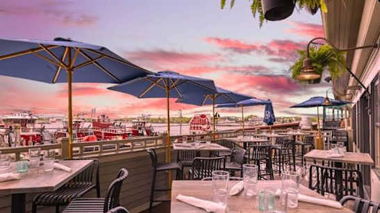 A restaurant with tables and chairs under umbrellas with a view of the water.