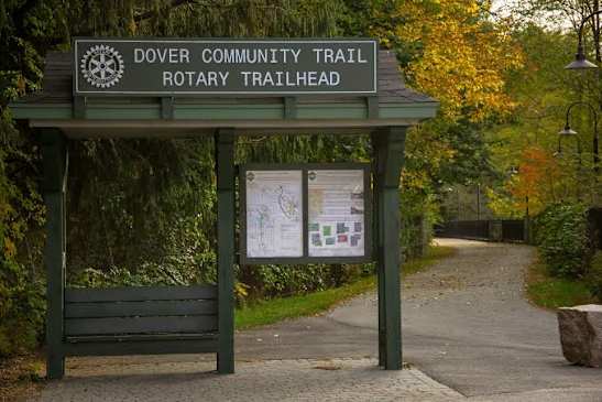 A sign for the Dover Community Trail Rotary Trailhead stands in front of a leafy path.