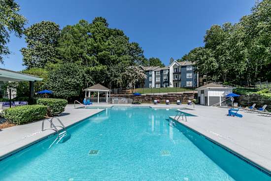 A large swimming pool surrounded by trees and a building in the background.