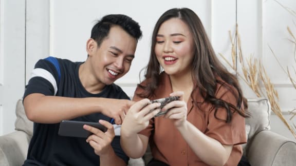 a man and woman sitting on a couch looking at a cell phone
