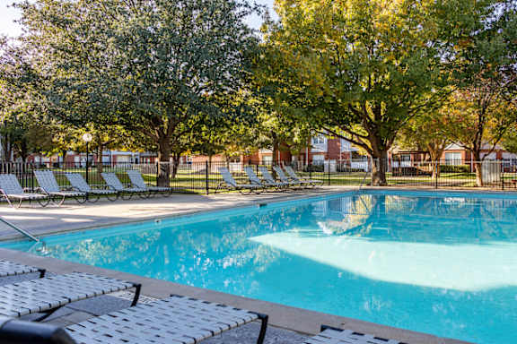 A swimming pool surrounded by trees and lounge chairs.