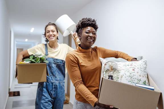 Two women carrying boxes with items in them.