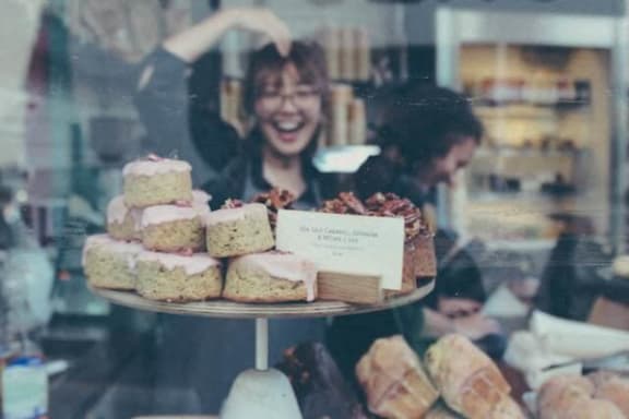 a woman is laughing behind a display of cakes