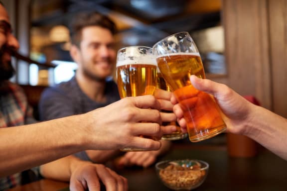 three people holding up glasses of beer at a bar