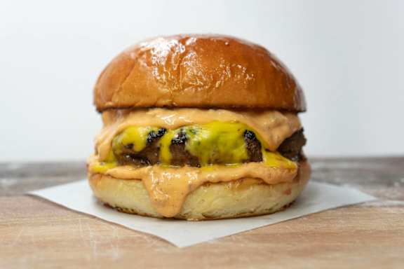 A burger with cheese and sauce on a wooden table.