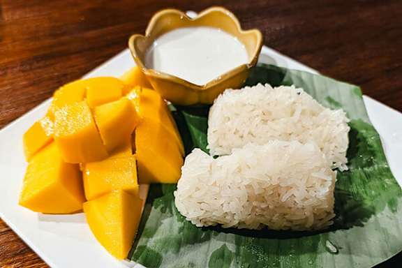 A plate of food with mango, rice, and a bowl of sauce.