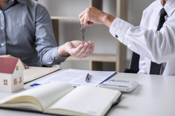 a man sitting at a desk handing over a set of keys to another man