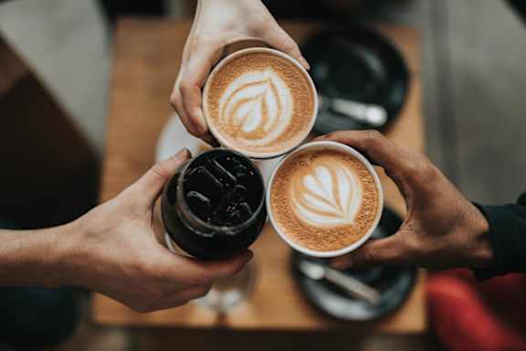 Three hands holding cups of coffee with latte art on top.