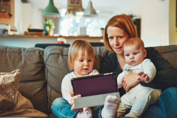 A woman and two children are sitting on a couch with a tablet.