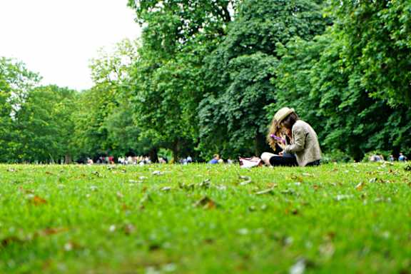 A woman is sitting on the grass in a park, reading a book.