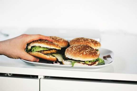 A hand is holding a plate with four burgers on it.