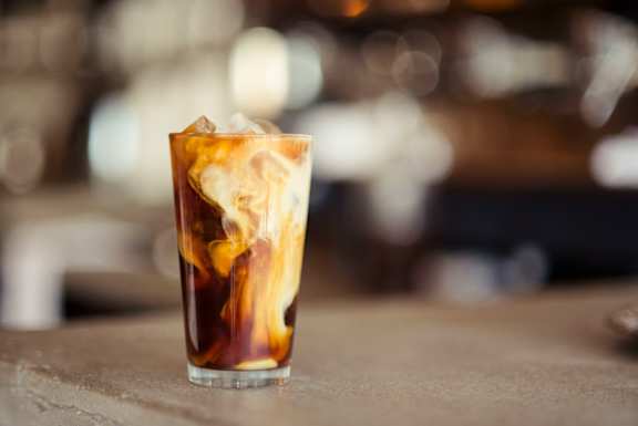A glass of iced coffee with ice cubes on a table.