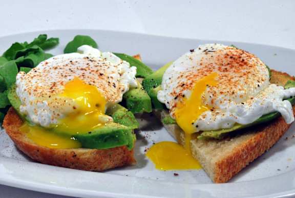 a white plate topped with eggs and avocado on toast