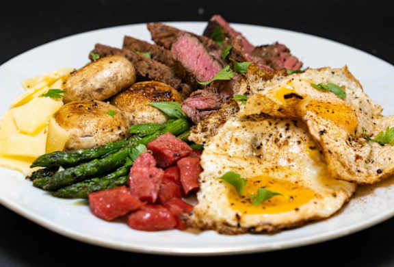 A plate of food with eggs, potatoes, asparagus, and meat.
