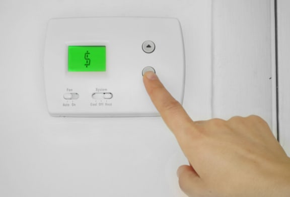 a hand pressing a button on a thermostat with a dollar sign