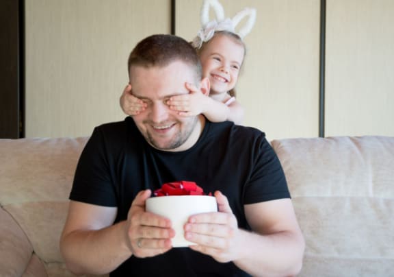 a man sitting on a couch holding a gift with a little girl on his shoulder