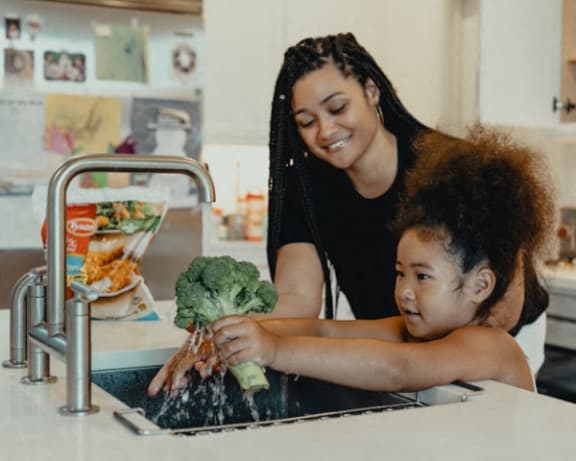a woman and a child washing vegetables in the kitchen sink