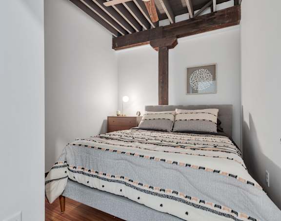 A bed with a wooden frame and a striped comforter is in a room with white walls.