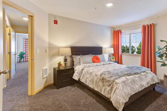 A bedroom with a bed, nightstand, and window with red curtains.