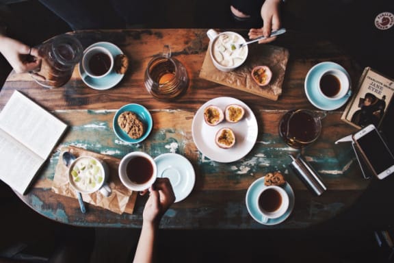 people sitting around a table with cups of coffee and food