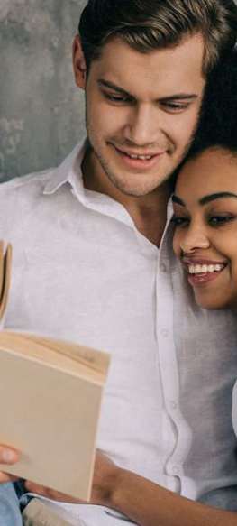 a man and woman sitting on a couch reading a book