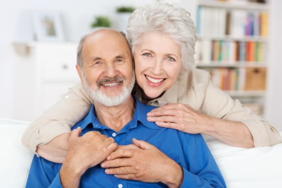 an elderly couple sitting on a couch with their arms around each other