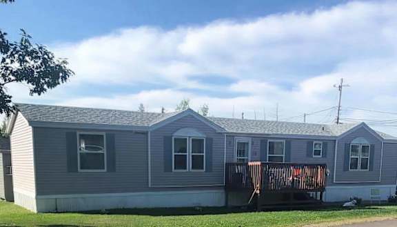 A grey mobile home with a deck and a tree in the background.