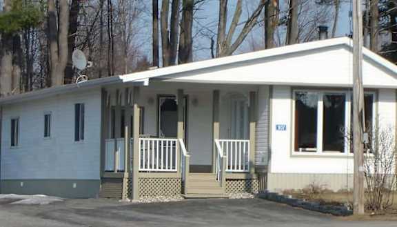 A small white house with a porch and a satellite dish on the roof.
