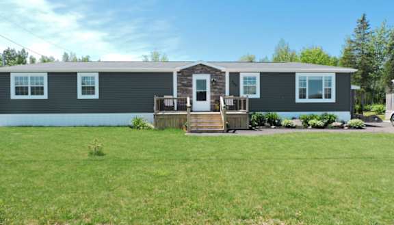 A green manufactured home with trees and a yard in front of it