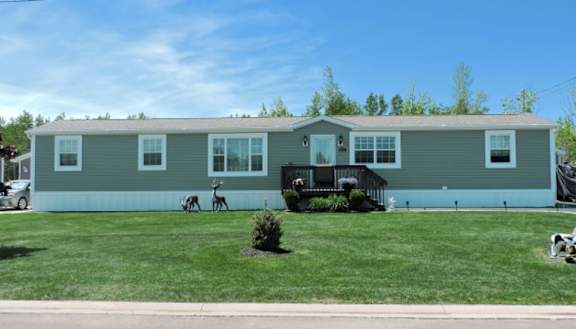 A green manufactured home with trees and a yard in front of it