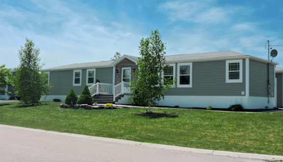 A green manufactured home with trees and a yard in front of it