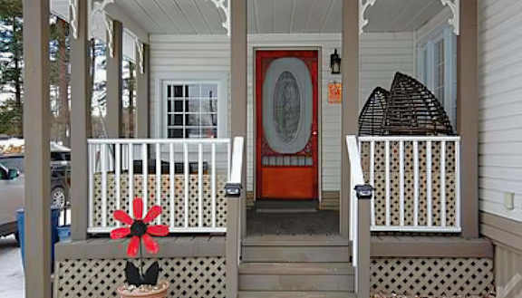 A red door is on the right side of a white porch.
