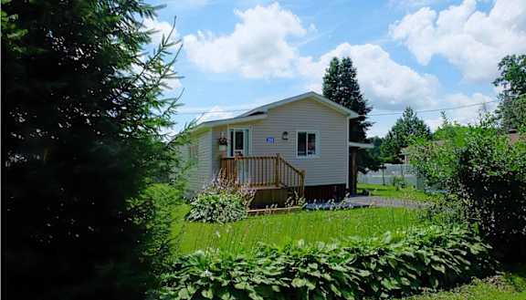 A small house with a porch surrounded by greenery.
