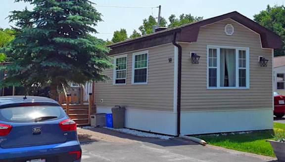 A small beige house with a blue car parked in front.