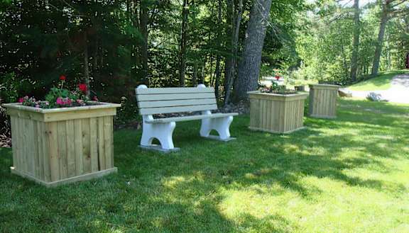 A white bench sits in the middle of a grassy area with wooden planters on each side.