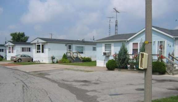 A series of blue manufactured homes with a driveway in front of each of them