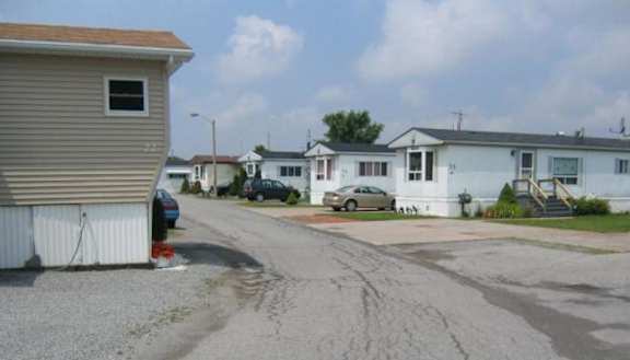 A residential street with houses on both sides and cars parked in front.