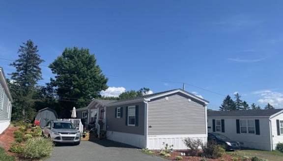 A manufactured home with grey walls and a car parked in front of it