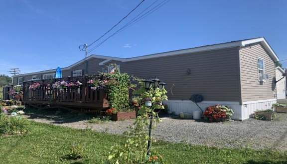 A house with a grey siding and a white door is surrounded by a gravel path and a garden with red flowers.