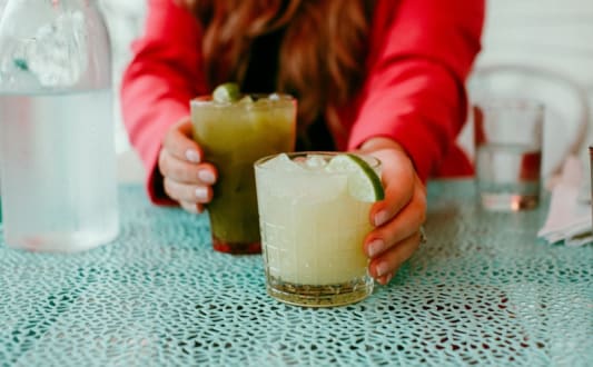 a woman holding two cocktails on a table