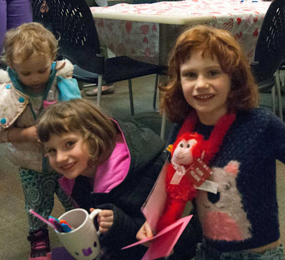 A young girl with red hair is holding a stuffed animal and smiling at the camera.