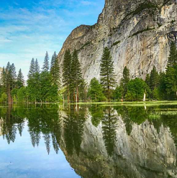 A serene lake surrounded by trees and a rocky cliff.