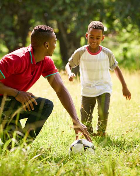 A man and a boy are playing with a soccer ball in a grassy field.